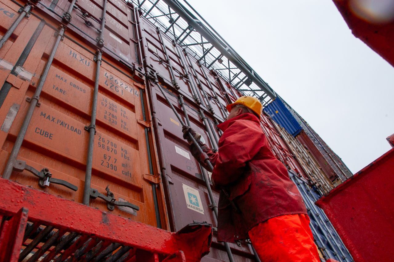 Home Industrial worker securing cargo containers on a rainy day at a shipping port.