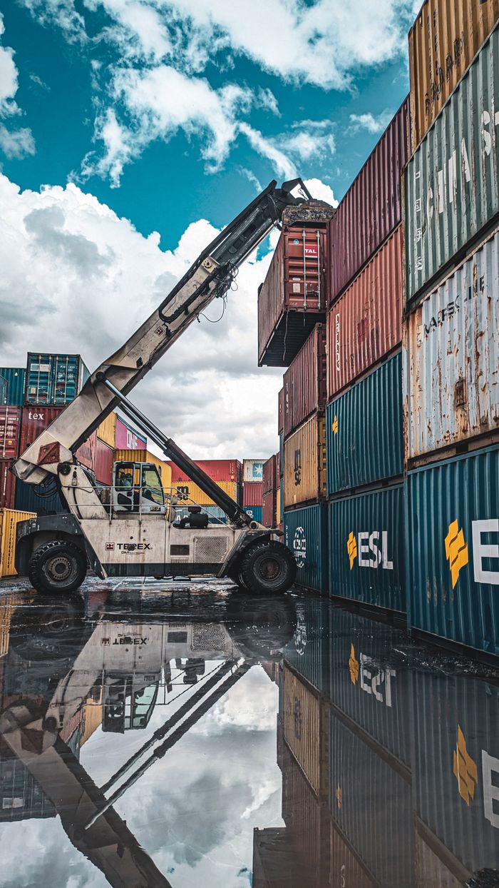 About A crane loader stacking colorful shipping containers at a port with reflection in water.